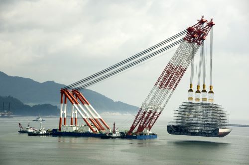 Floating crane on body of water with mountains in background.